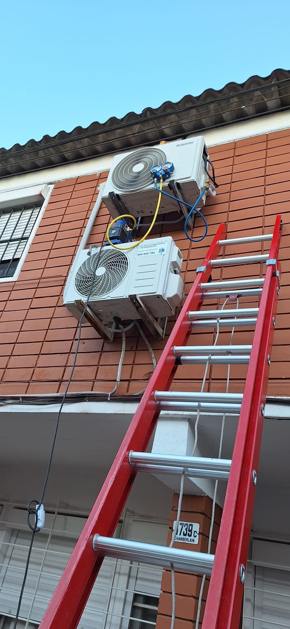 Dos unidades exteriores instaladas una sobre otra en la fachada de una casa, con el manómetro y la bomba de vacío conectados y una escalera apoyada.