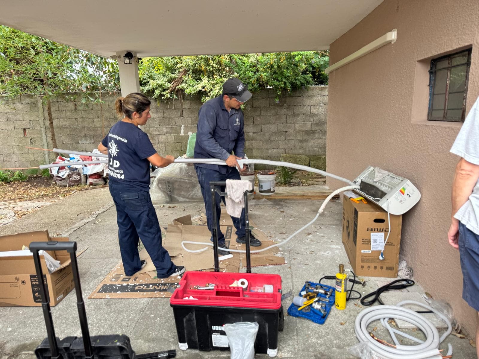 Dos personas del equipo de J&D preparando la cañería de cobre aislada en el patio de una casa, con las herramientas y la bomba de vacío desplegadas en el piso.