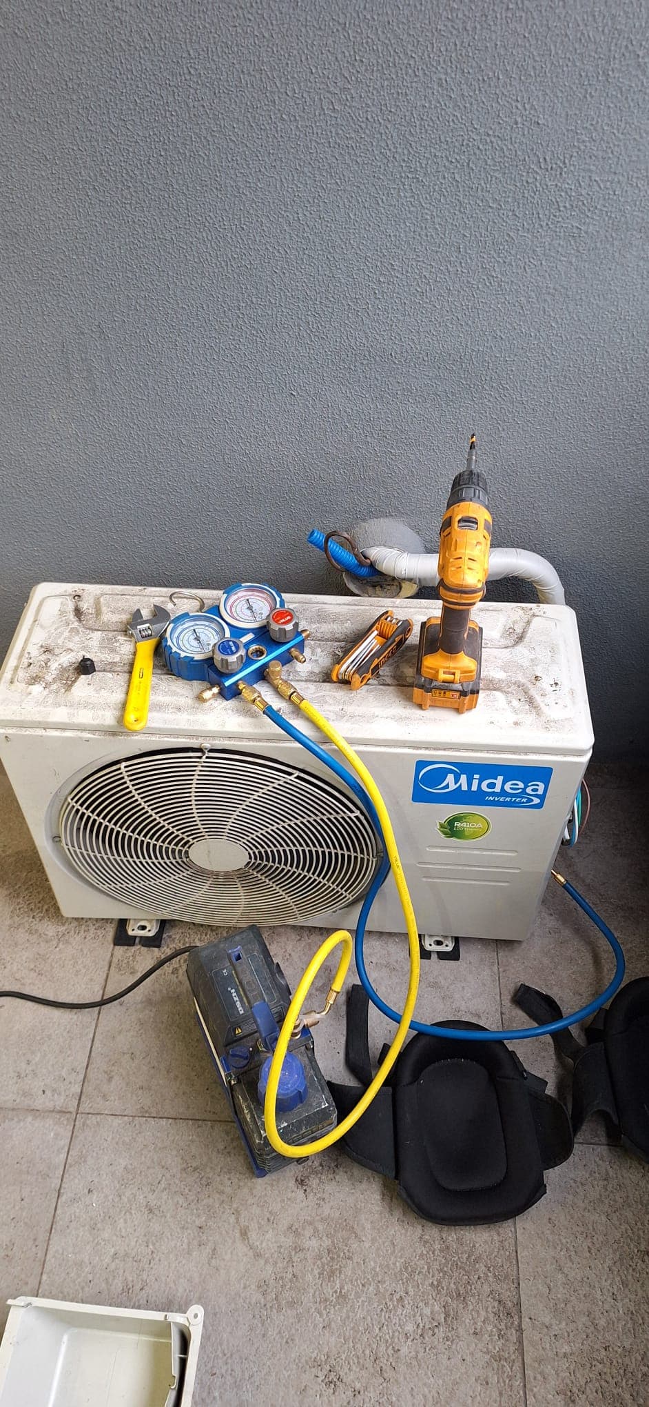 Service de una unidad exterior Midea Inverter, con el manómetro y la bomba de vacío conectados y las herramientas apoyadas sobre el equipo.