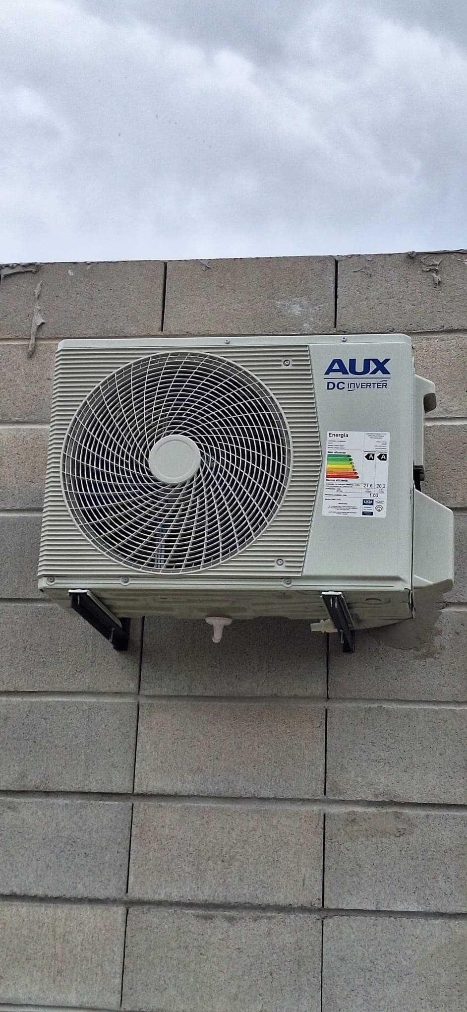 Unidad exterior AUX DC Inverter instalada sobre una pared de bloques, nivelada y con el desagüe colocado.